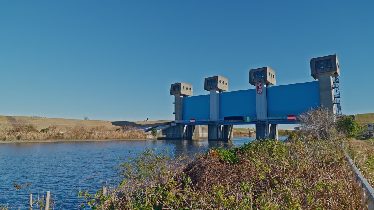 A wide shot of the iconic Iwabuchi Water Gate, also known as the "Blue Sluice," located on the Arakawa River in Tokyo. This massive blue steel infrastructure serves as a crucial flood control system