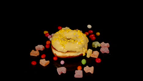 yellow funny surprised glazed donut with sprinkles, striped caramel candies, colorful dragee with raisins or peanuts inside rotate on black background