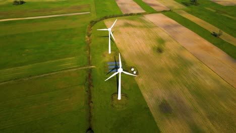 drone shot of two working wind turbines and a few solar panels producing green electric energy on a cultivated field on a sunny summer day, use of renewable resources of energy, parallax