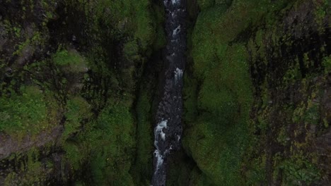 Río-De-Montaña-Que-Fluye-Entre-Acantilados-Cubiertos-De-Musgo,-Vista-Aérea-Hacia-Abajo-En-La-Cascada-De-Glymur,-Islandia