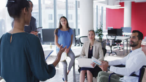 Mixed-race-businesswoman-holding-file-and-talking-to-diverse-colleagues-at-casual-office-meeting