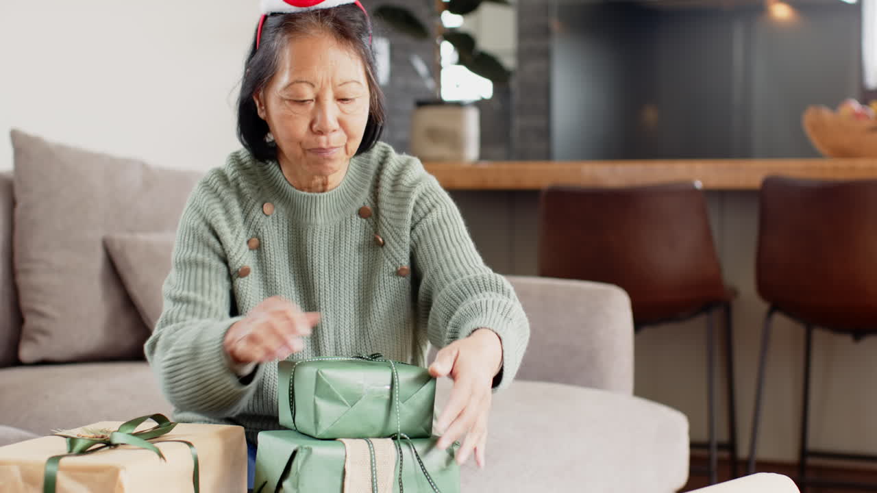 Smiling senior woman wrapping Christmas gifts at home, enjoying festive season