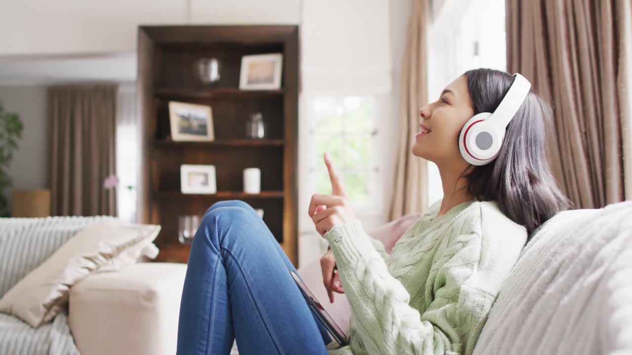 헤드폰 과 스마트폰 을 사용하는 어두운 머리카락 을 가진 미소 짓는 두 인종 의 여성 의 비디오