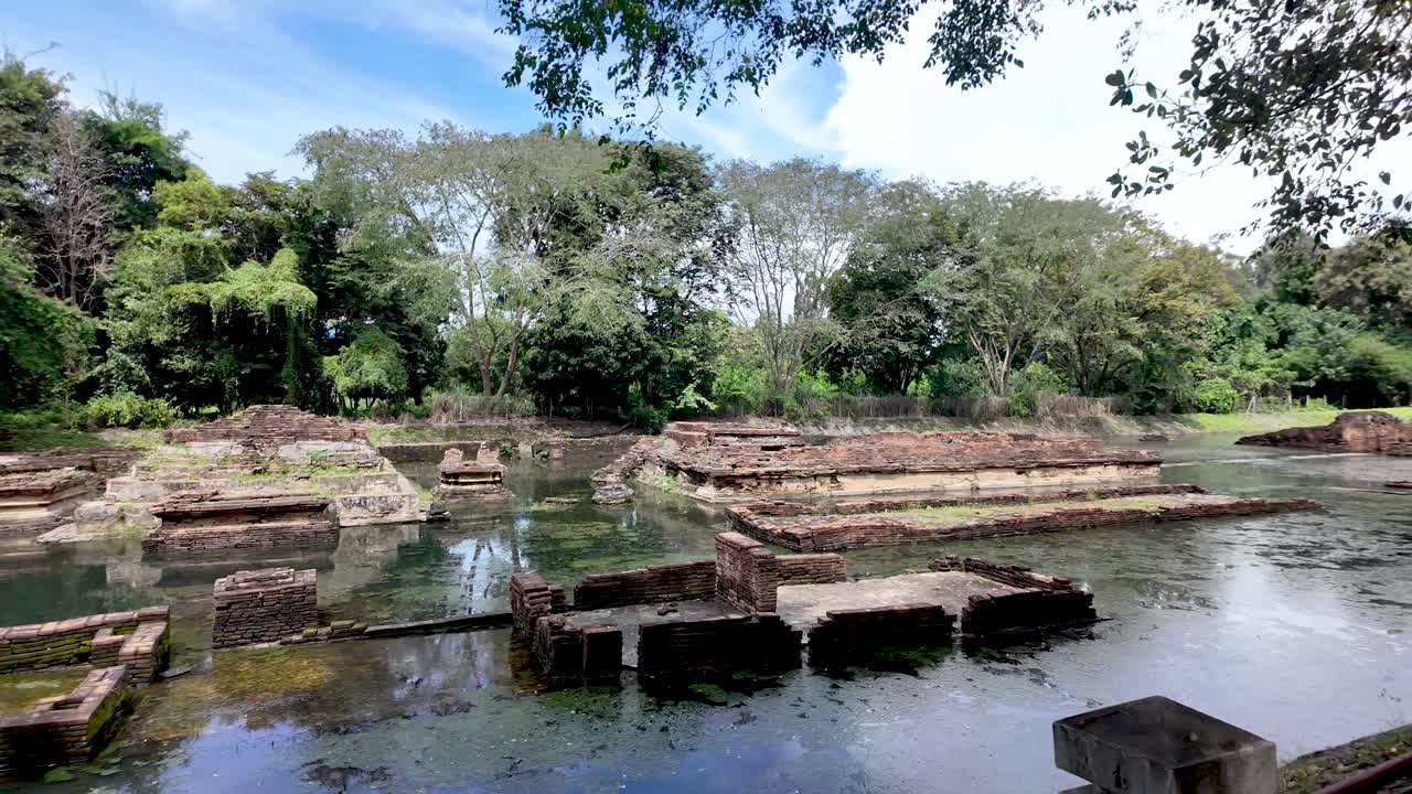 Wat Nan Chang ancient Buddhist temple ruins surrounded by water and lush green trees in Thailand