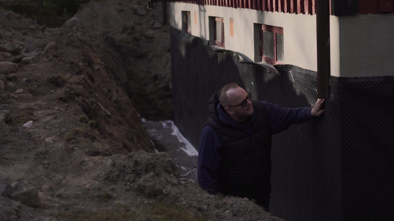 Il proprietario di casa osserva gli appaltatori installare l'isolamento su una parete esterna di una casa durante lavori di ristrutturazione residenziale o di miglioramento energetico