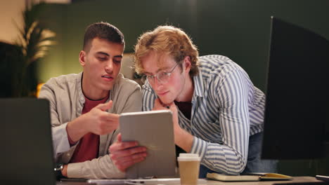 Two men working together on a tablet in an office