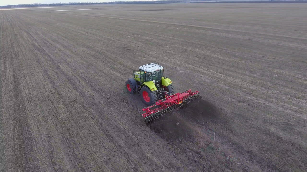 항공 추적 비디오: 트랙터가 필드의 토양을 처리하고 프레임의 대각선을 따라 이동합니다.