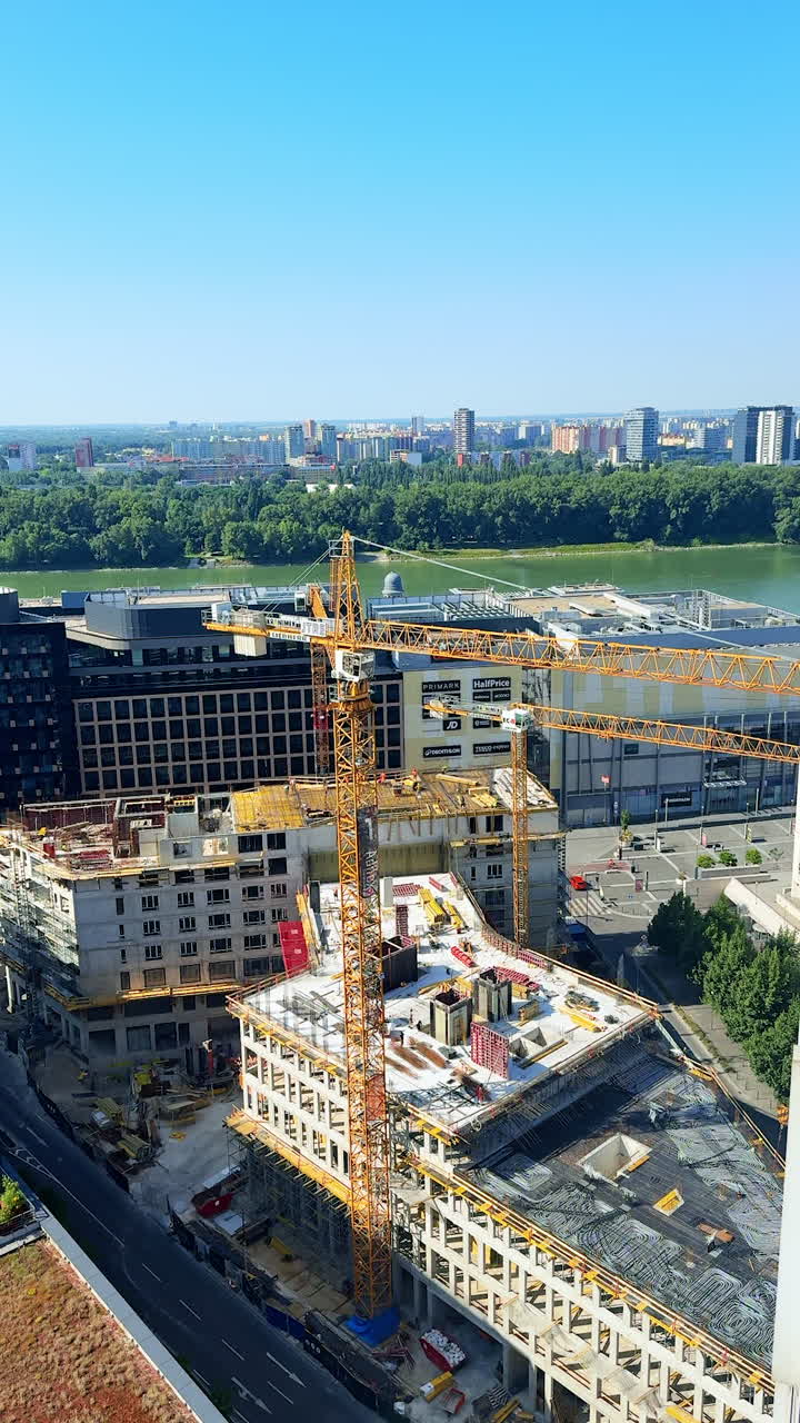 City construction site viewed from above. A bustling construction site reveals cranes and building activity near a river in a vibrant urban area on a sunny day