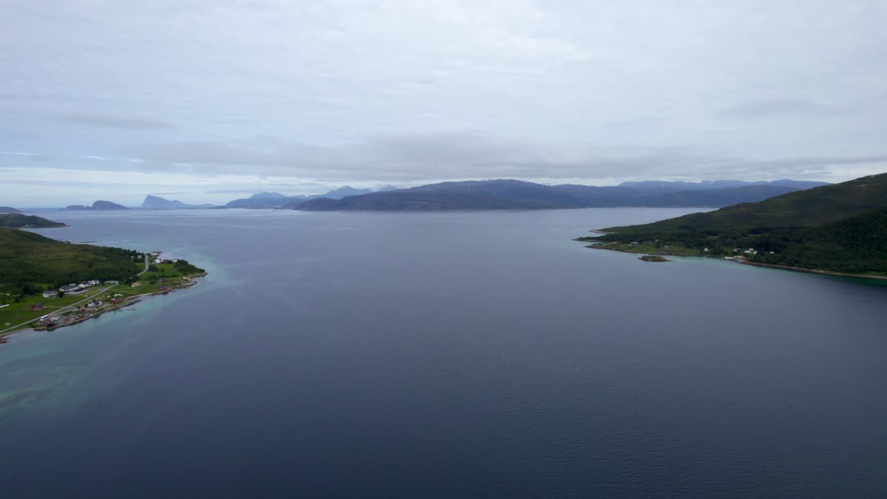 Reversing aerial dolly shot across the waterway between the islands of kval&oslash;ya and Senja on a slightly overcast day with a small boat traveling across the water