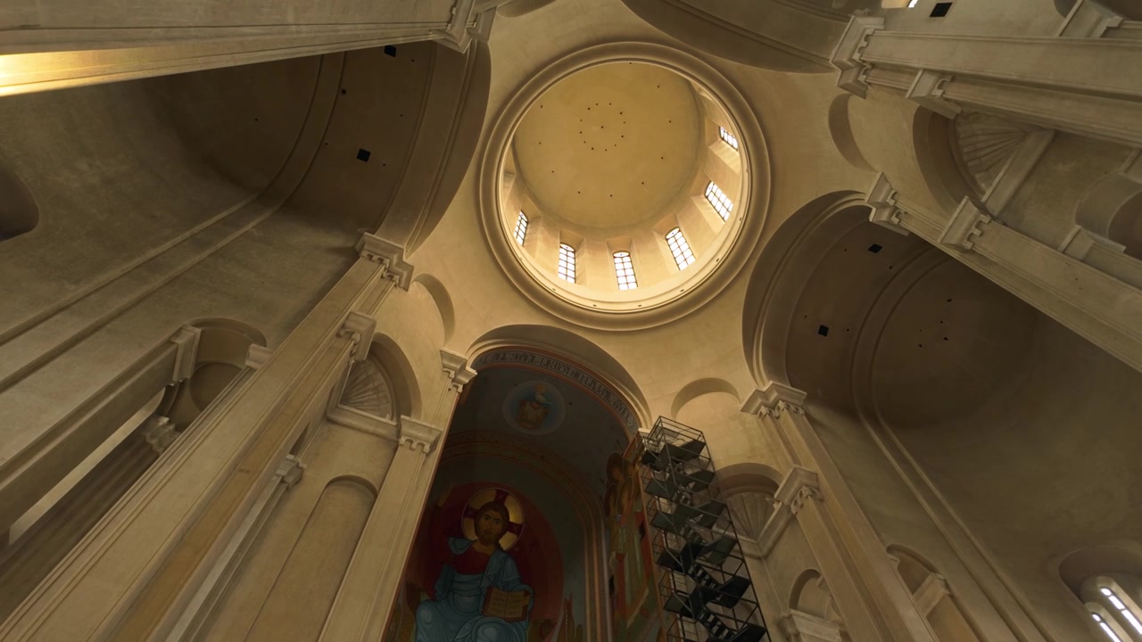 Expansive interior view of the Holy Trinity Cathedral in Tbilisi, Georgia, capturing the grandeur of its dome, towering pillars, and vibrant religious frescoes decorating the walls and ceiling.