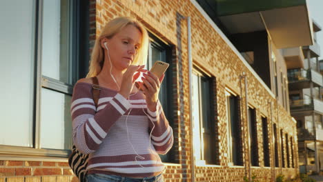 a young woman is using the application on a smartphone standing by a beautiful brick building at sun