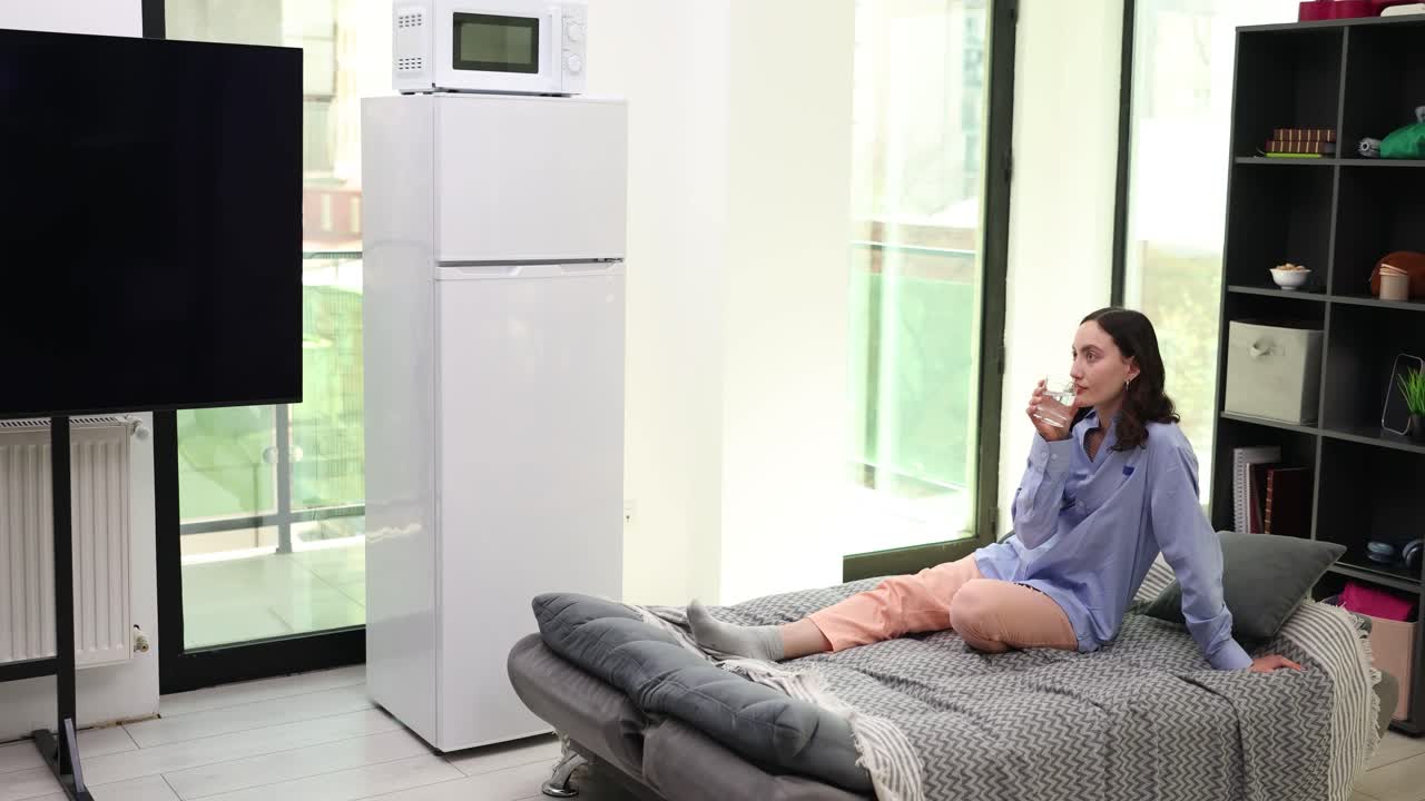 A woman is sitting on the bed and drinking water