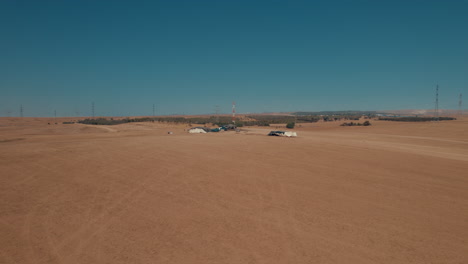 bedouin tents in an arid and remote area, on a dry sand field off the grid, near large power lines and an animal feed factory-parallax shot