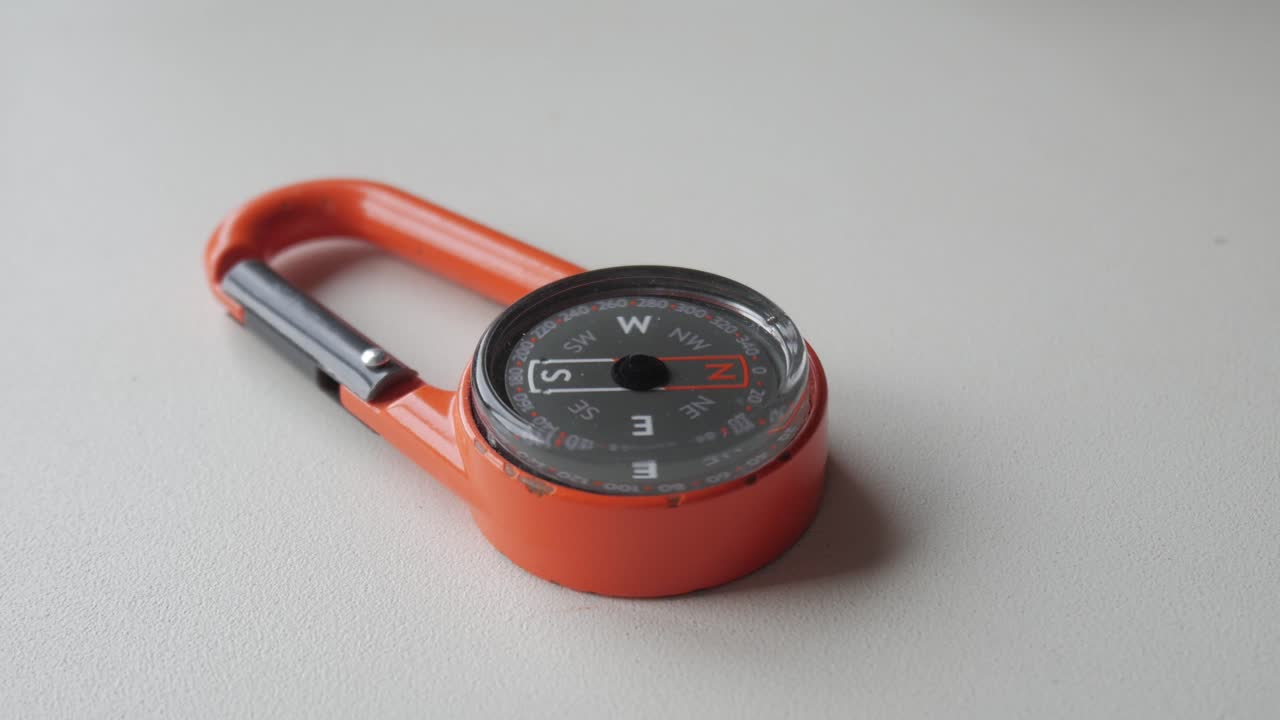 Bright orange compass carabiner lying on a light surface, symbolizing direction and travel
