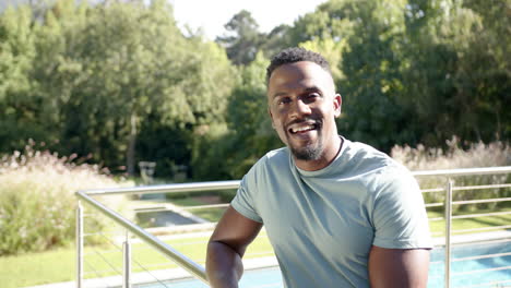 smiling man sitting by home pool, enjoying sunny day outdoors