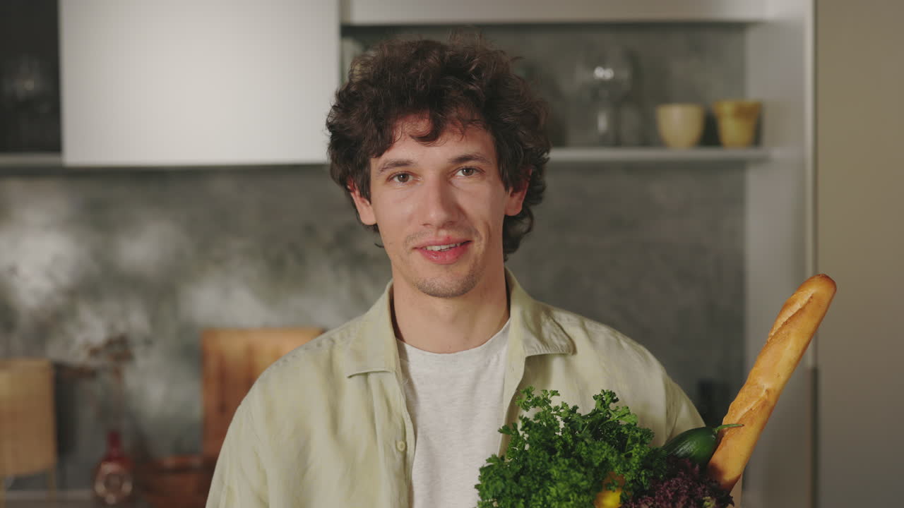 A young man holds a bag of groceries with fresh produce in a modern kitchen