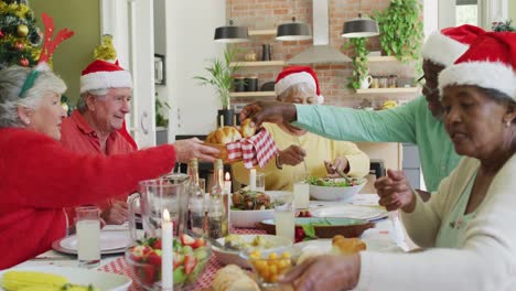 grupo de felices y diversos amigos mayores con sombreros de santa haciendo un brindis en la mesa de la cena de navidad en casa
