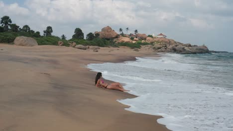 Aerial-view-of-sand-beach-at-sunset-with-beautiful-young-slim-woman-sunbathing-lying-on-a-beach