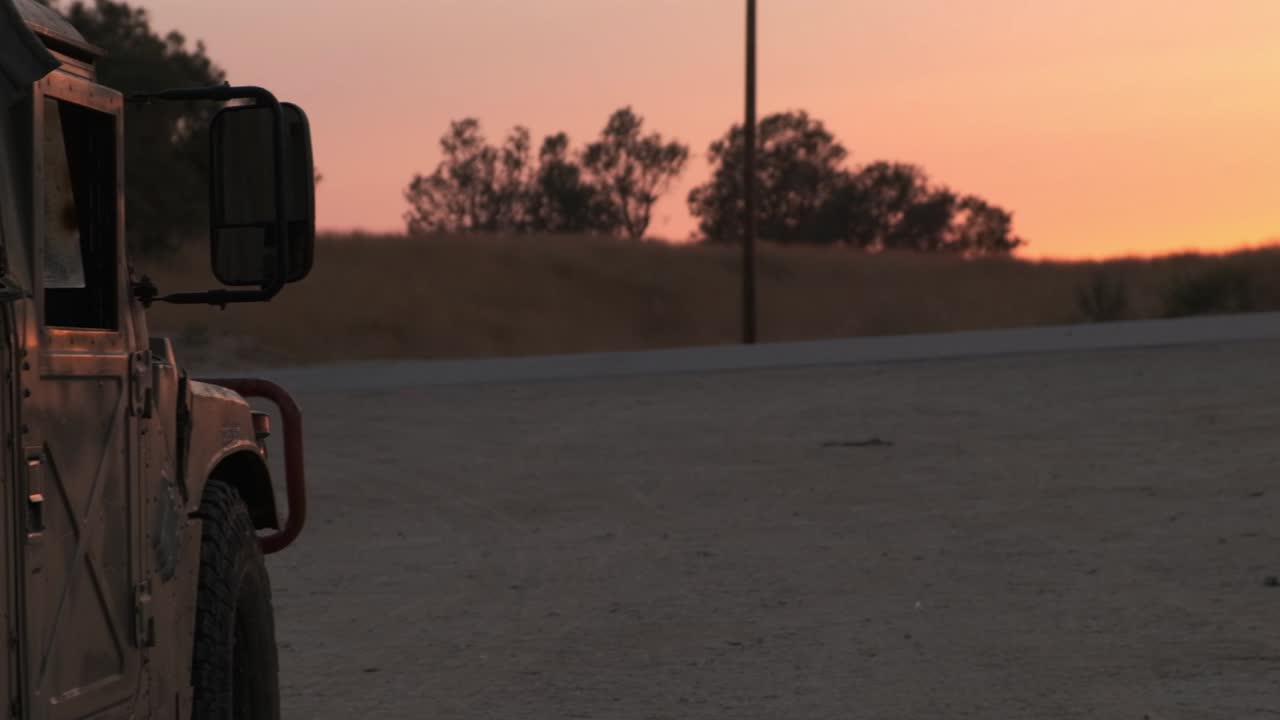 close-up of Military army Hummer Vehicle in the middle of the desert during the amazing orange sunset next to a field