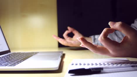 young female hands doing yoga on a minimal office workplace with a laptop, a notebook and a pen, for stress relief during work