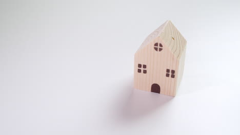 wooden toy house casting shadow on the table and then the lefthand fingers pushing in a red toy sportscar next to the toy house