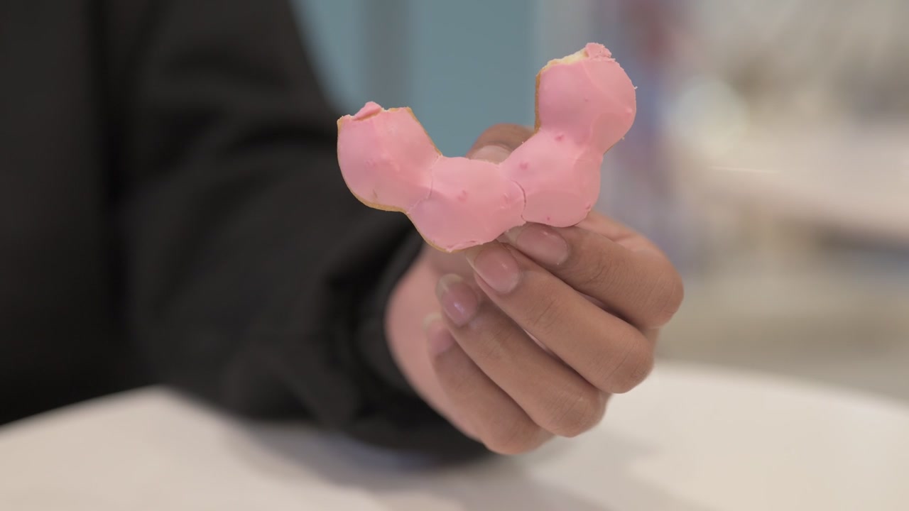 Close-up of hand holding half of pink donut