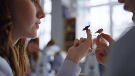 un primer plano de una mujer y un hombre sosteniendo insectos en un entorno de aula