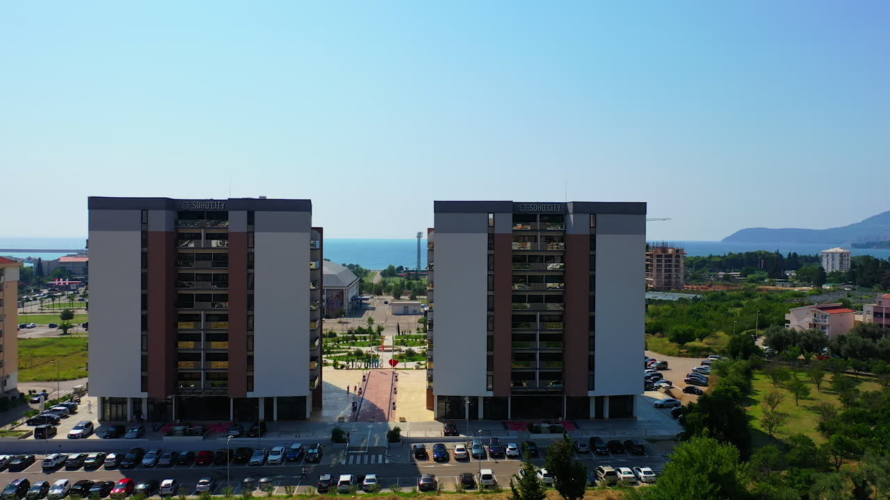 Flying between the similar beautiful buildings in the cityscape of Bar, Montenegro. Lovely green area at the shore of Adriatic Sea from air.