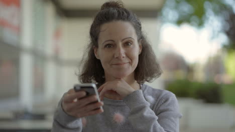 Mujer-Sonriente-De-Mediana-Edad-Usando-Un-Teléfono-Inteligente-En-La-Calle.