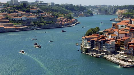 Boats-passing-on-Douro-River-in-Porto,-Portugal-4K-SLOWMO-CINEMATIC-AERIAL-SUMMER-MEDITERRANEAN-CITY-RIVERSIDE