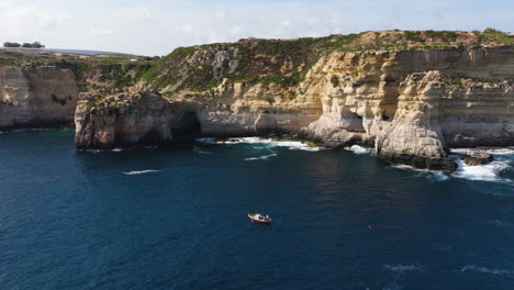 aerial view around a boat on the steep, rocky coastline of the sunny malta island