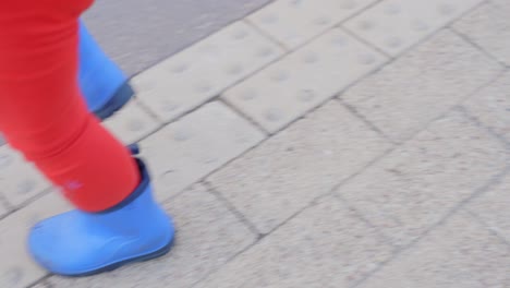 little child walking wearing blue shoes in city landscape, legs shot