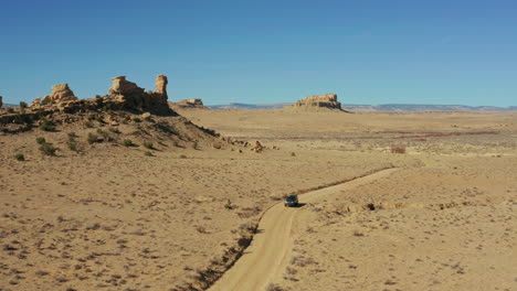 aerial as car drives across open desert with rock formations in distance