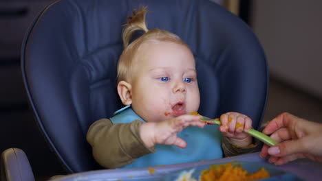 adorable caucasian baby takes the spoon from mom's hand. little kid puts the spoon to his mouth. close up.