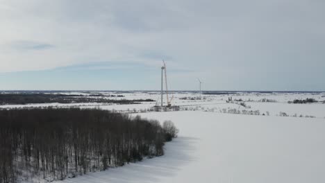 drone flying over snow covered farm fields with wind farm and windmills on horizon