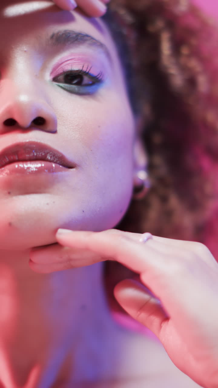 Vertical video of biracial woman with dark hair in blue and pink light, slow motion