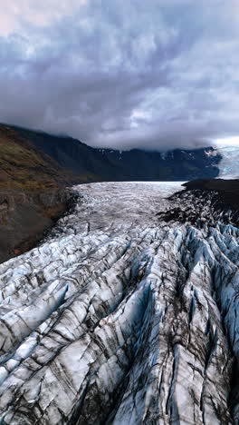 ridges of marble glacier in the valley among the mountains. dramatic cloudscape hanging over the rocks. iceland scenery. vertical video.