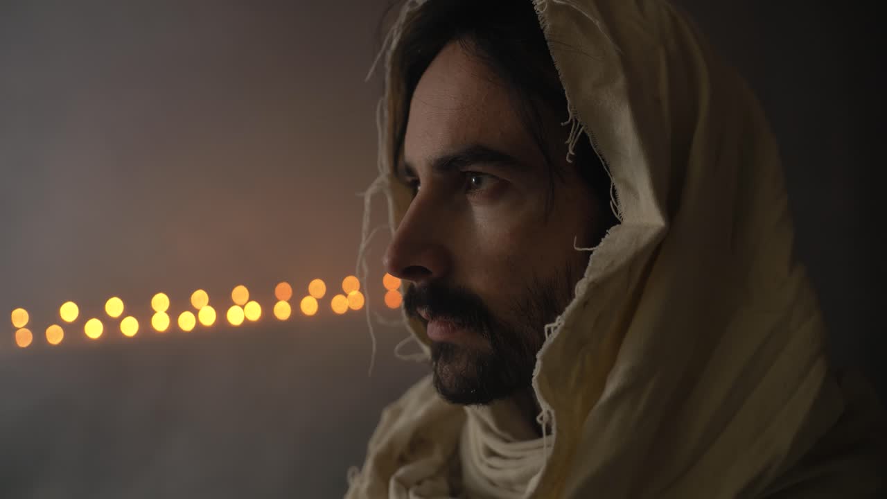 Closeup of Jesus Christ in prayer, in ambient light, with candlelight in the distant background for cinematic and dramatic Christian stock footage. Perfect for church, worship, easter, and Sunday