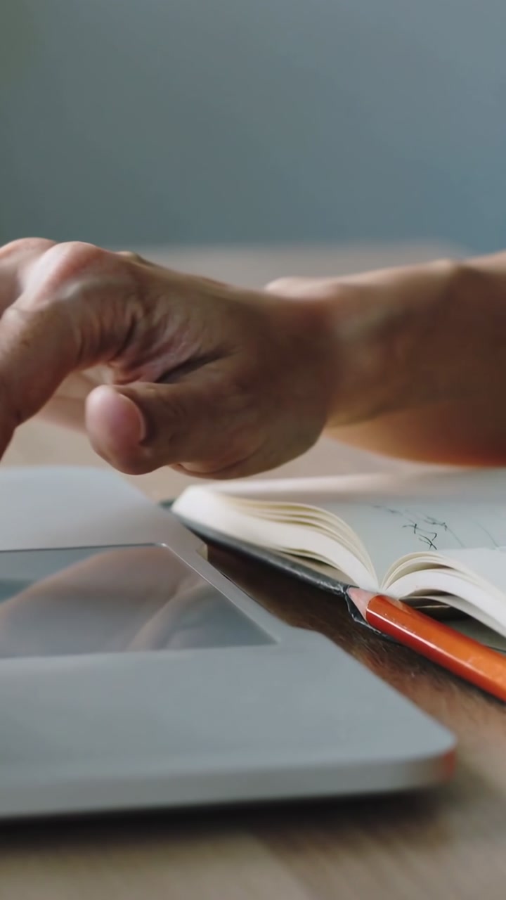 Vertical video: Hovering hand tapping and swiping laptop trackpad at desk, notebook, orange pencil