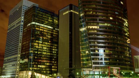 Timelapse-of-three-modern-skyscrapers-at-night,-featuring-glass-facades,-illuminated-interiors-and-unique-color-patterns-on-each-facade