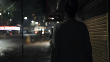 Woman-walking-in-city-nighttime-slow-motion-bokeh-lights-illuminated-shop-signs