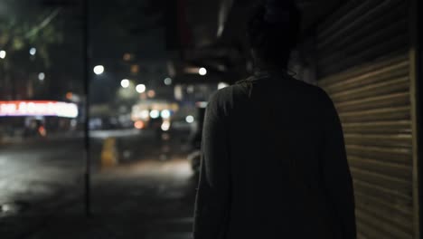 woman walking in city nighttime slow motion bokeh lights illuminated shop signs