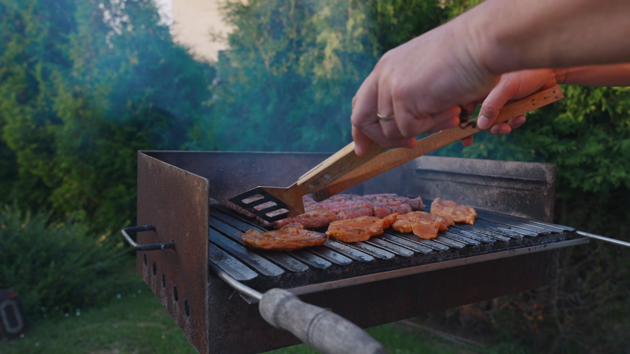 Person flipping meat on barbecue with spatula in outdoor backyard setting