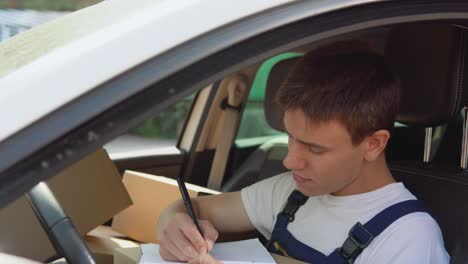 Moving and delivery of manufactured goods. The courier fills in the cargo documents. Many craft boxes are stacked in the passenger seat next to the driver. Delivery of goods home