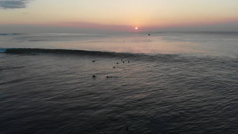 increíble toma aérea de un surfista montando una ola de 5-6 pies en bali, mar abierto, grupo de surfistas y puesta de sol en el fondo