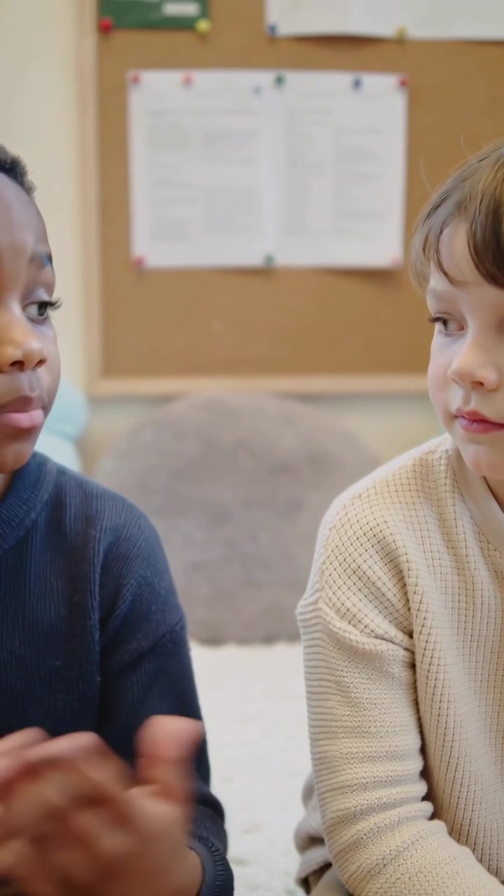 Vertical video: Starting left kid navy sharing and gesturing, peer listening in play corner, board