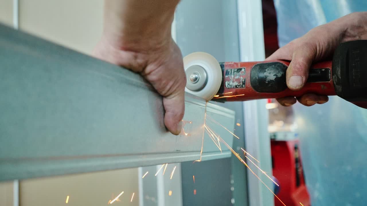 Close-up of craftsman slicing metal by hand with red power tool and visible sparks