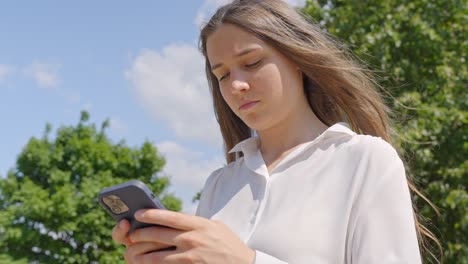 bruneta elegante con una mirada seria comprobando el teléfono inteligente en un día soleado