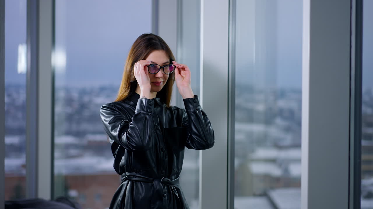 Businesswoman in a black leather dress with glasses by the window