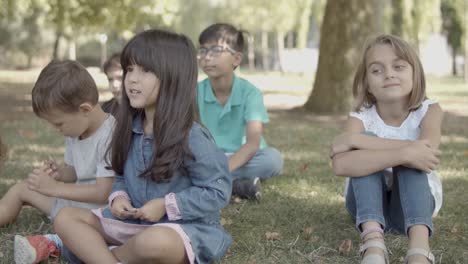 niñas y niños multiétnicos sentados juntos en el césped en el parque